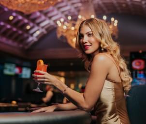 A woman wearing a dress sitting at the casino bar drinking a cocktail