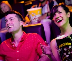 Couple sitting in a movie theater laughing and eating popcorn