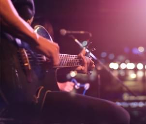 A musician playing a guitar, sitting on a stage in front of a microphone