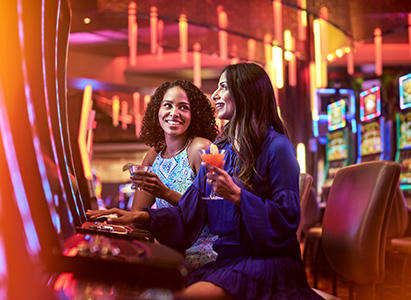 Two women with cocktails playing slot machines
