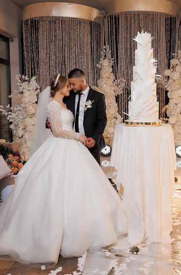 Bride and groom posing next to their wedding cake.